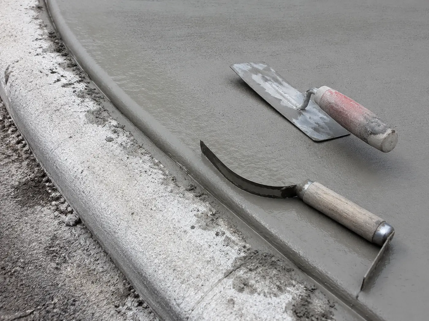 Edging tool on the wet transition where a new driveway apron meets a municipal curb